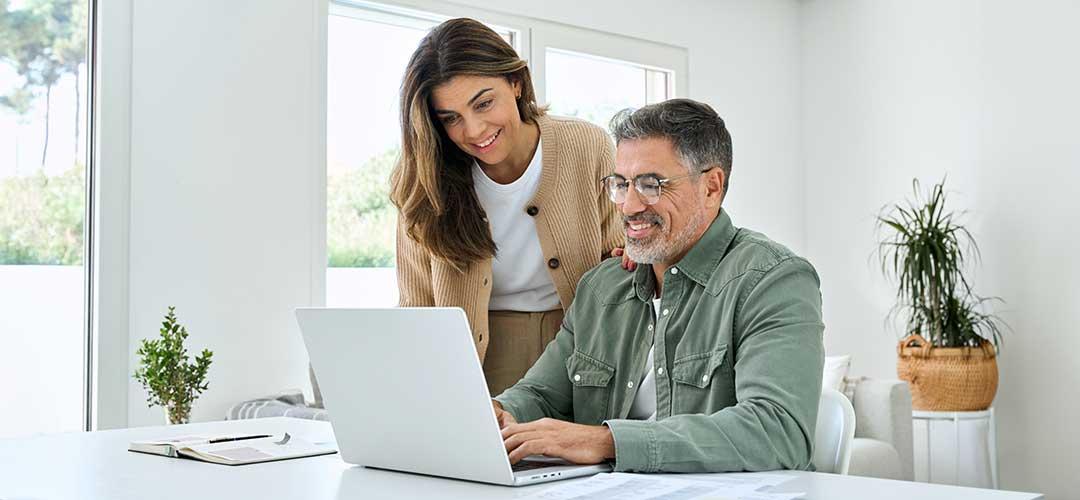 Middle aged couple using laptop at kitchen table